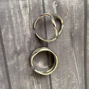 May include: Two silver rings, one with a simple round shape and the other with a unique open design.