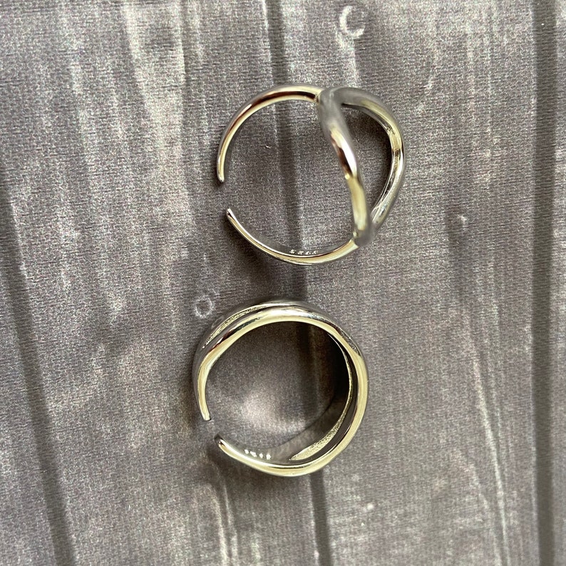 May include: Two silver rings, one with a simple round shape and the other with a unique open design.