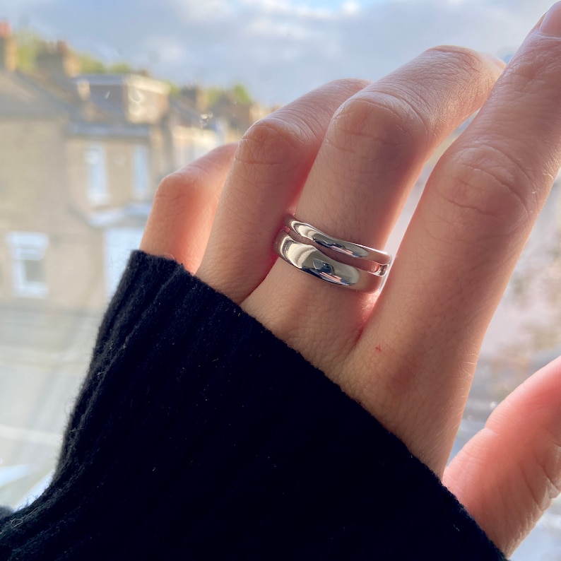 May include: Two silver rings stacked on a finger. The rings are both smooth and have a rounded shape.