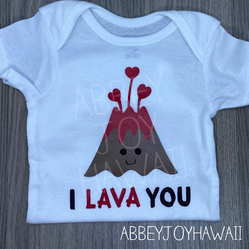May include: White baby onesie featuring a brown and red volcano with a smiling face and red hearts erupting from the top. The text "I lava you" is printed in black and red on the onesie.