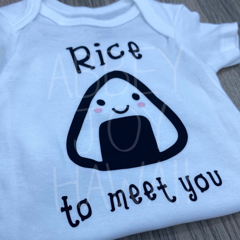 May include: White baby onesie with a black and white illustration of a smiling rice ball with the text "Rice to meet you".