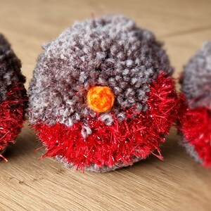May include: Three grey and red pom-pom ornaments shaped like robins with orange beaks.