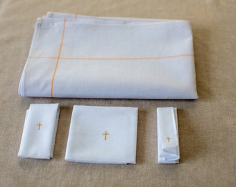 Puede incluir: Juego de manteles y accesorios de altar de lino blanco. El juego incluye un paño grande doblado con líneas de acento naranja, dos paños rectangulares doblados, un paño cuadrado y un paño doblado con una cruz dorada bordada en cada uno.