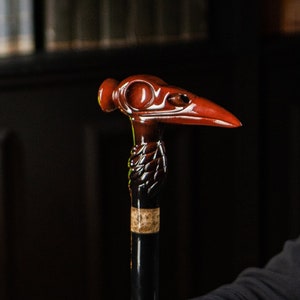Pode incluir: Bengala preta com punho em forma de cabeça de pássaro. O cabo é de cor castanho-avermelhada e o eixo é preto. A bengala tem uma secção decorativa e texturizada perto do topo. Um acessório elegante.