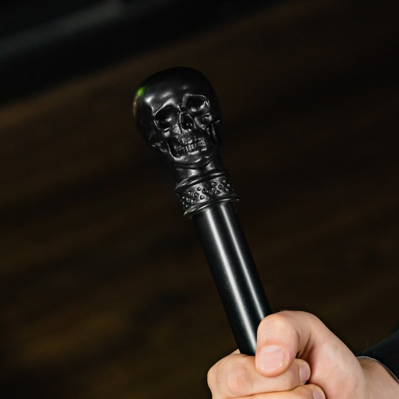 May include: A black skull-shaped walking stick with a detailed design. The stick is made of a smooth, black material and has a textured grip.