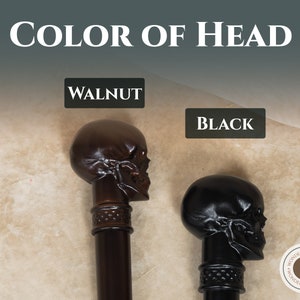 May include: Two skull-shaped walking stick heads, one walnut brown and one black. The heads are shown against a beige background. The text "COLOR OF HEAD" is at the top of the image. The text "WALNUT" is above the brown skull and the text "BLACK" is above the black skull.