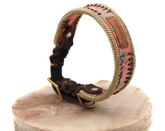 May include: A pink and turquoise dog collar with a brown leather strap and a gold buckle. The collar has a rope design and a leather tag with the text "Wanderlust" in cursive.