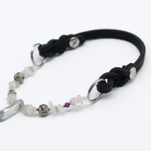 K&ouml;nnte beinhalten: Ein schwarzes Lederhundekragen mit geflochtenem Design und silberner Hardware. Das Halsband hat einen Kristallanh&auml;nger und eine Kette aus bunten Perlen.