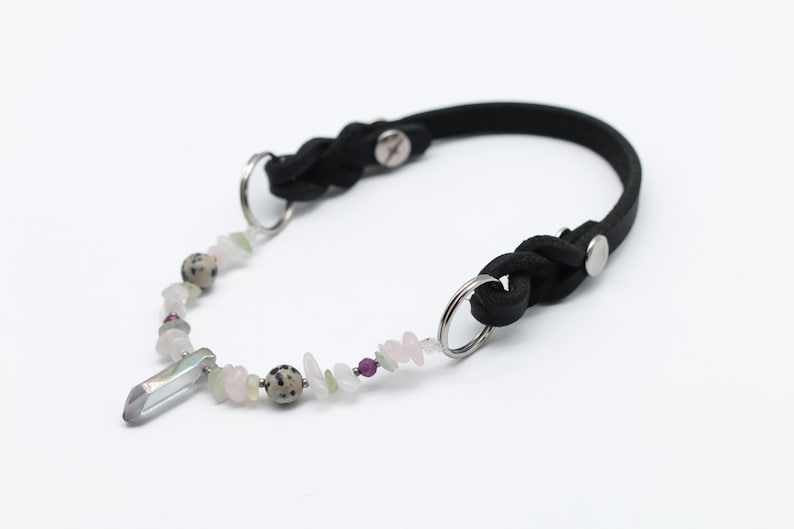 K&ouml;nnte beinhalten: Ein schwarzes Lederhundekragen mit geflochtenem Design und silberner Hardware. Das Halsband hat einen Kristallanh&auml;nger und eine Kette aus bunten Perlen.