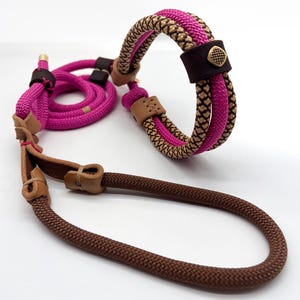 Könnte beinhalten: Ein Hundeleinen- und Halsbandset aus geflochtenem Seil mit leuchtend pinken und beigen Mustern. Das Set enthält braune Seilabschnitte, hellbraune Lederakzente und ein kleines quadratisches, messingfarbenes Metallemblem auf einer dunkelbraunen Lederschlaufe.