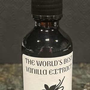 May include: A dark glass bottle of vanilla extract with a black dropper. The label reads "The World's Best Vanilla Extract" with a vanilla flower and Farmer Mick's Provisions. The bottle is on a speckled surface.