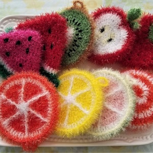 May include: A collection of colorful crocheted fruit-shaped dishcloths, including watermelon, strawberry, apple, kiwi, lemon, lime, and orange.