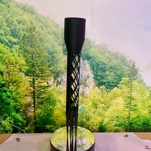 Puede incluir: Un portavelas decorativo negro con un patrón de diamantes y una base de espejo. El portavelas tiene un diseño alto y esbelto con una parte superior cilíndrica y una sección media en forma de celosía. La base tiene un interruptor de encendido/apagado.