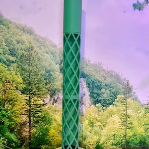 Puede incluir: Un objeto decorativo verde y alto con una parte superior cilíndrica y un cuerpo enrejado con diseño de diamantes. El objeto se apoya sobre una base circular. El diseño es moderno y geométrico, con enfoque en el espacio abierto y patrones repetidos.