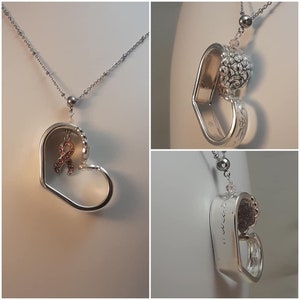 May include: A silver heart-shaped pendant necklace with a delicate chain. The pendant features a heart design with a pink ribbon charm and a decorative spoon element. The necklace is displayed against a neutral background.
