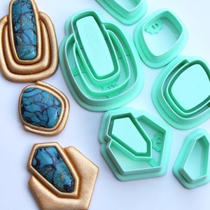 Op de afbeelding: Drie goudkleurige geometrische vormen met ingelegde blauw en zwart gemarmerde steenachtige centra, vergezeld door zes mintgroene plastic uitsteekvormen in bijpassende vormen, waaronder rechthoekige, vierkante en zeshoekige contouren.