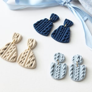 Könnte beinhalten: Drei Paar Hängeohrringe mit einer Strickstruktur. Die Ohrringe sind in drei Farben: marineblau, hellblau und beige.