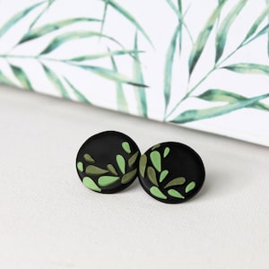 Könnte beinhalten: Ein Paar runde Ohrstecker in Schwarz und Grün mit einem Blattmotiv.