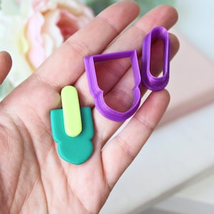 Può includere: Un set di tre stampini per biscotti in verde, giallo e viola. Gli stampini hanno la forma di un ghiacciolo, un cuore e un rettangolo.