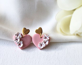 May include: A pair of pink heart-shaped earrings with white flower accents and gold heart-shaped posts.