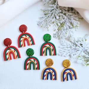 Könnte beinhalten: Eine Sammlung bunter Polymer Clay Ohrringe im Regenbogen-Design. Die Ohrringe haben einen glitzernden kreisförmigen Aufsatz und eine gebogene Regenbogenform mit roten, grünen, weißen, goldenen und blauen Farben. Festlicher und dekorativer Schmuck.