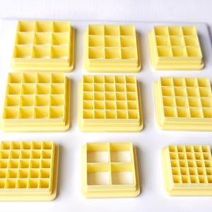 Può includere: Una collezione di nove tagliapasta a griglia in plastica gialla disposti in una griglia tre per tre. Ogni tagliapasta presenta una cornice quadrata o rettangolare distinta divisa in scomparti interni per creare vari motivi.