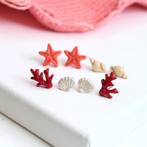 May include: A set of six polymer clay earrings featuring a variety of sea-themed designs. The earrings include two red coral branches, two white seashells, and two red starfish.