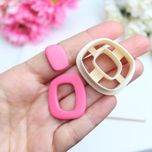 Könnte beinhalten: Ein Set aus drei Teilen, bestehend aus einem kleinen rosa abgerundeten Rechteck, einem größeren rosa abgerundeten Rechteck mit offener Mitte und einem cremefarbenen Kunststoff-Ausstecher mit passender Form.