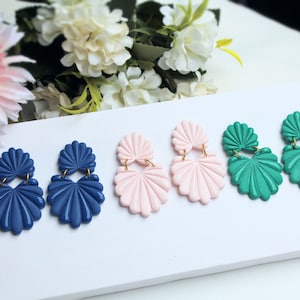 Könnte beinhalten: Vier Paar Hängeohrringe mit Muschel-Design. Die Ohrringe sind in Blau, Rosa und Grün.