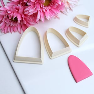 Pode incluir: Quatro cortadores de biscoitos de madeira em forma de arco, com um recorte de fondant rosa em forma de arco.