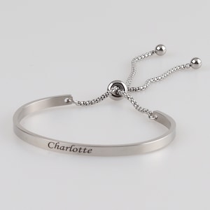 May include: A silver bracelet with a sliding adjustable clasp and the name "Charlotte" engraved on the band.