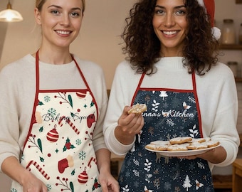 Può includere: Due donne in cucina con grembiuli. Un grembiule è bianco sporco con rifiniture rosse e un motivo natalizio, l'altro è blu navy con un motivo natalizio. Una donna indossa un cappello da Babbo Natale. I grembiuli hanno il testo "Baking Squad" e "Anna's Kitchen".
