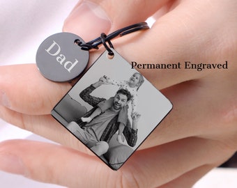 May include: Black metal keychain with a square photo charm featuring a father and daughter. The photo charm is engraved with the words "Permanent Engraved". A round charm with the word "Dad" is attached to the keychain.