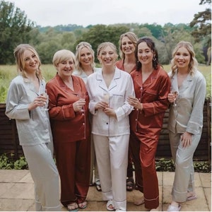 May include: Seven people wearing matching pajamas in different colors. The pajamas are long-sleeved and have a button-up front. The people are smiling and holding glasses of champagne.