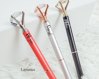 May include: Three personalized pens with diamond-shaped tops. The pens are silver, black, and coral with gold accents. The names "Megan", "Sarah", and "Mike" are engraved on the pens.