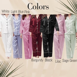 Puede incluir: Conjuntos de pijama de sat&eacute;n en varios colores: blanco, azul claro, rosa, burdeos, negro, lila y verde salvia. Cada conjunto presenta una camisa con botones con ribete en contraste y pantalones a juego. La palabra "Colors" se muestra en la parte superior.