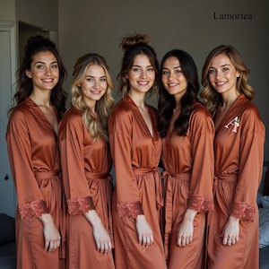 Può includere: Cinque donne con abiti in raso color ruggine abbinati con finiture in pizzo sulle maniche. Ogni abito ha una cintura abbinata. Un abito ha un'iniziale ricamata. Gli abiti sono di Lamoriea.