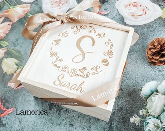 May include: A wooden box with a light brown ribbon tied around it. The box is engraved with the letter "S" surrounded by a floral design and the name "Sarah". The ribbon is labelled "Gifts for loved ones" and "Lamoriea".