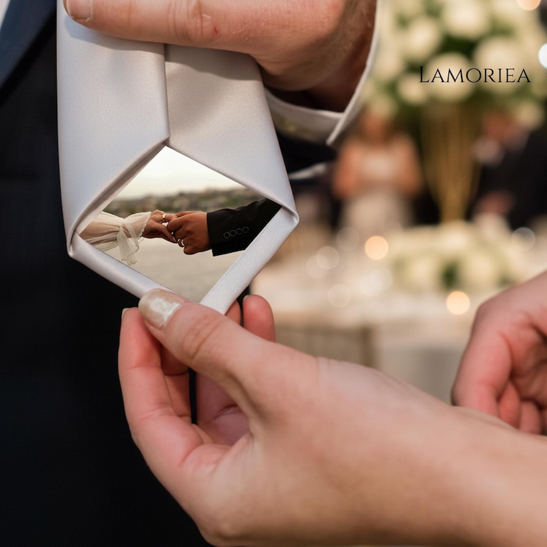 May include: A solid white necktie featuring a custom photo print of a couple holding hands with wedding rings visible. The fabric is smooth and matte, and the brand name LAMORIEA is printed in the upper right corner of the image area.
