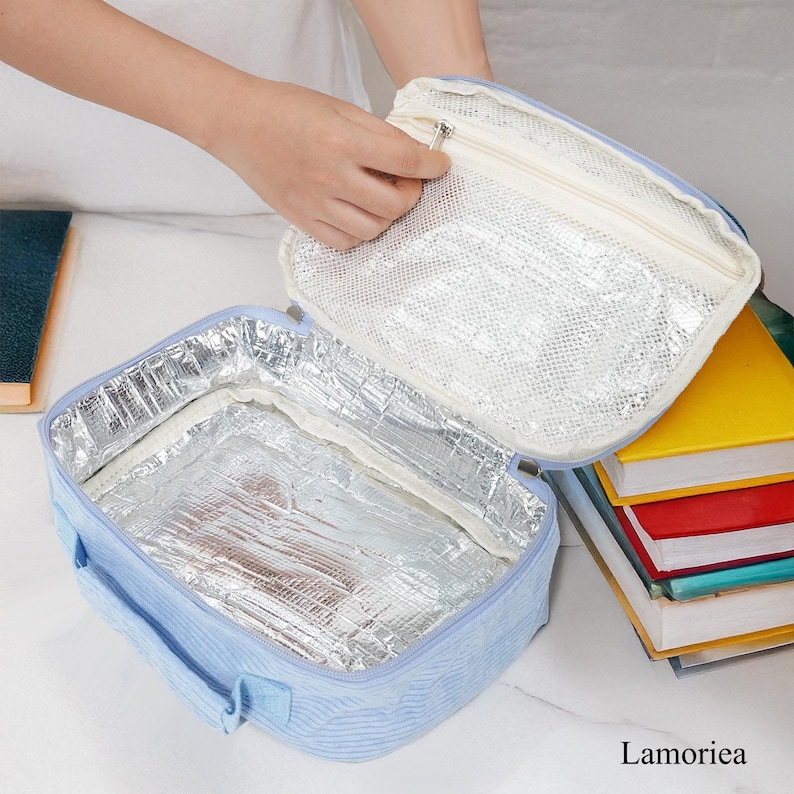 Pu&ograve; includere: Una borsa termica per il pranzo azzurra con un motivo a righe. La borsa &egrave; aperta, rivelando un interno isolato argentato e una tasca a rete nel coperchio. La borsa ha una chiusura a zip e un manico. La parola "Lamoriea" &egrave; nell'angolo in basso a destra.