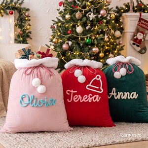 May include: Three plush velvet Christmas gift sacks with white faux fur trim and drawstring closures. The pink sack features the name Olivia, the red sack features the name Teresa with a hat icon, and the dark green sack features the name Anna.