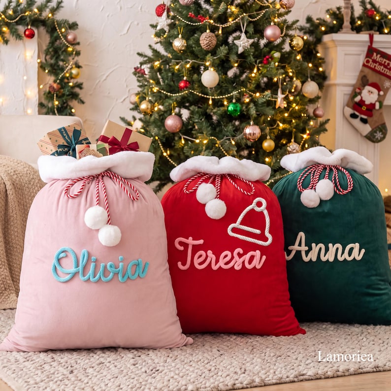 May include: Three plush velvet Christmas gift sacks with white faux fur trim and drawstring closures. The pink sack features the name Olivia, the red sack features the name Teresa with a hat icon, and the dark green sack features the name Anna.