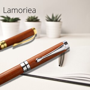 May include: Two wooden pens with gold and silver accents. The pens are on a white surface with a notebook.