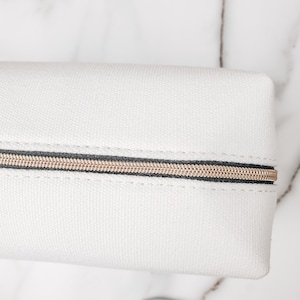 May include: White canvas zippered pouch with a gold zipper.