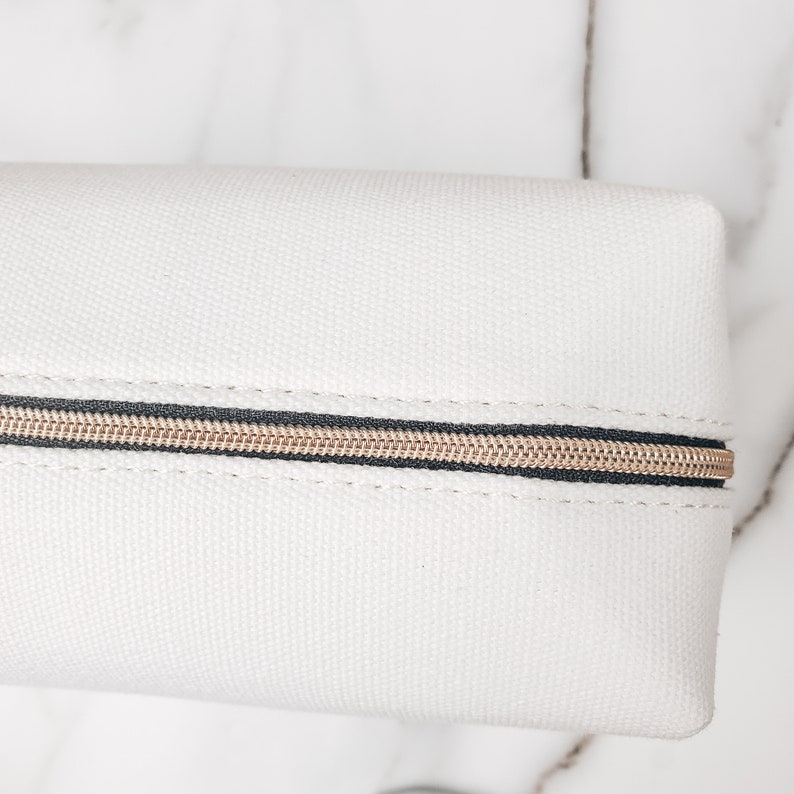 May include: White canvas zippered pouch with a gold zipper.