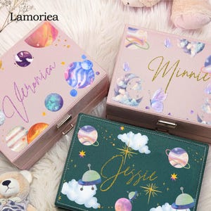 May include: Three decorative boxes with celestial designs. Two are pink with planets and the names "Veronica" and "Minnie" in gold script. The third box is green with planets, clouds, and the name "Jessie".