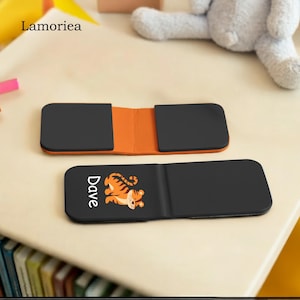Puede incluir: Cartera negra y naranja con un dise&ntilde;o de tigre y el nombre "Dave". La cartera est&aacute; abierta, revelando un interior naranja. La marca "Lamorea" es visible en la esquina superior izquierda.