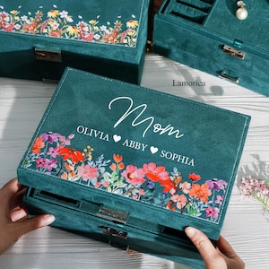 May include: Teal jewelry box with a floral design and the words "Mom, Olivia, Abby, Sophia" on the lid. The box has two drawers.