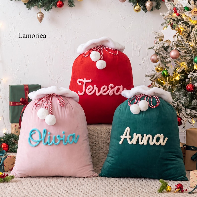 May include: Three plush Christmas gift sacks in red, pink, and dark green. Each sack features a white faux fur trim, a red and white drawstring with white pom-poms, and a personalized name in raised script: Teresa, Olivia, and Anna.