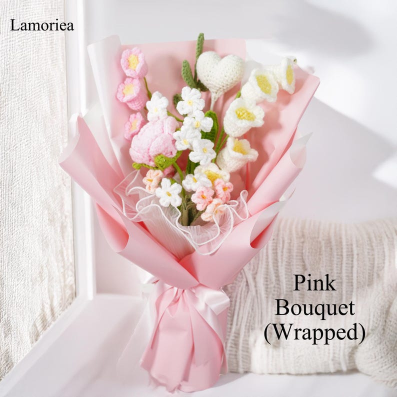 May include: A pink crocheted bouquet of flowers wrapped in pink tissue paper. The bouquet includes a pink rose, white flowers, and a white crocheted heart.